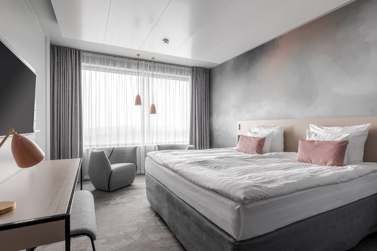 A modern hotel room with a large bed, a desk, and a chair.