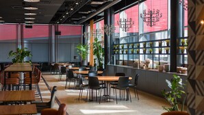 A modern dining area with multiple tables and chairs, large windows with potted plants, and a geometric wall design. - Break Sokos Hotel Flamingo (Vantaa)