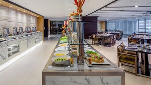 Een moderne eetruimte van een hotel met een buffetopstelling, marmeren aanrechtbladen en diverse gerechten.