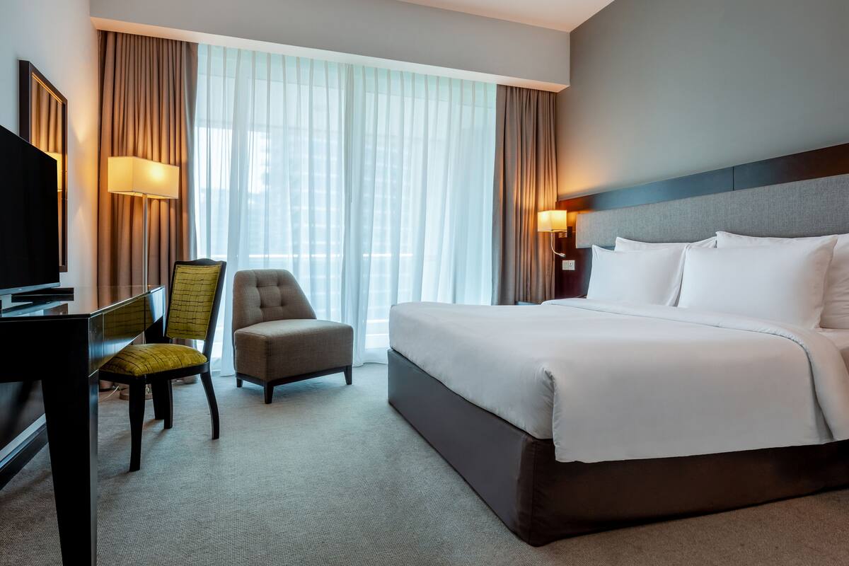 Een hotelkamer met een bed, een bureau met een televisie, een stoel en een lamp.
