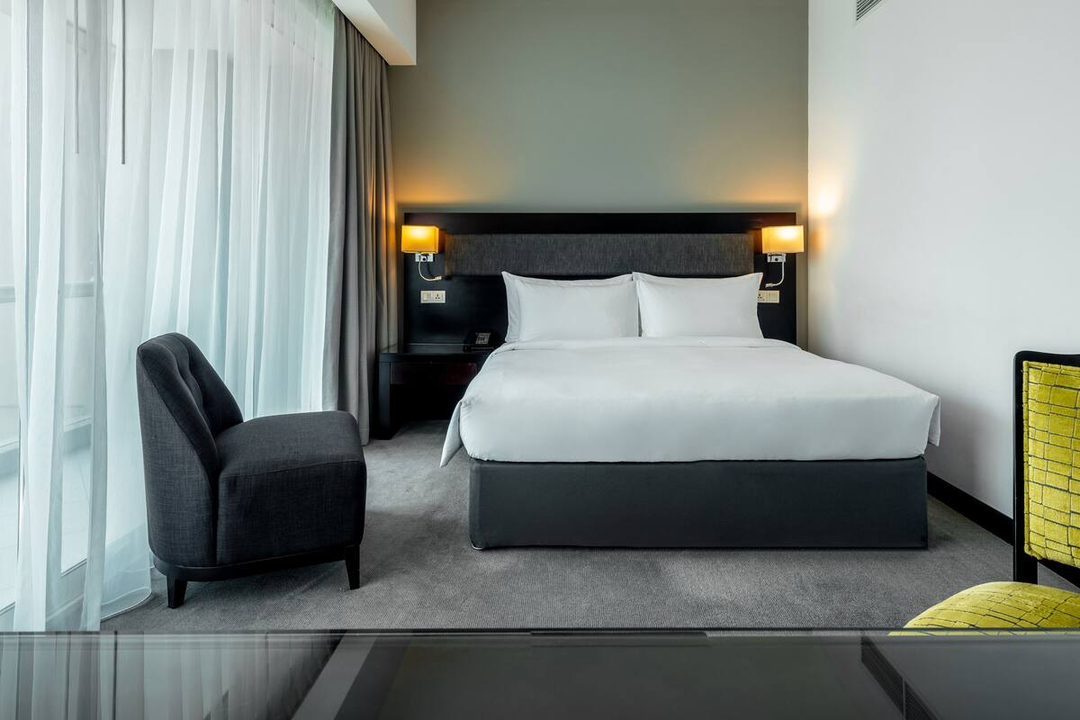 Een moderne hotelkamer met een groot bed, een stoel, een nachtkastje en een bureau met een stoel.