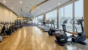 Een fitnessruimte met loopbanden, elliptische trainers en gewichtstoestellen, grote ramen met uitzicht over de stad, en een gebogen plafond.
