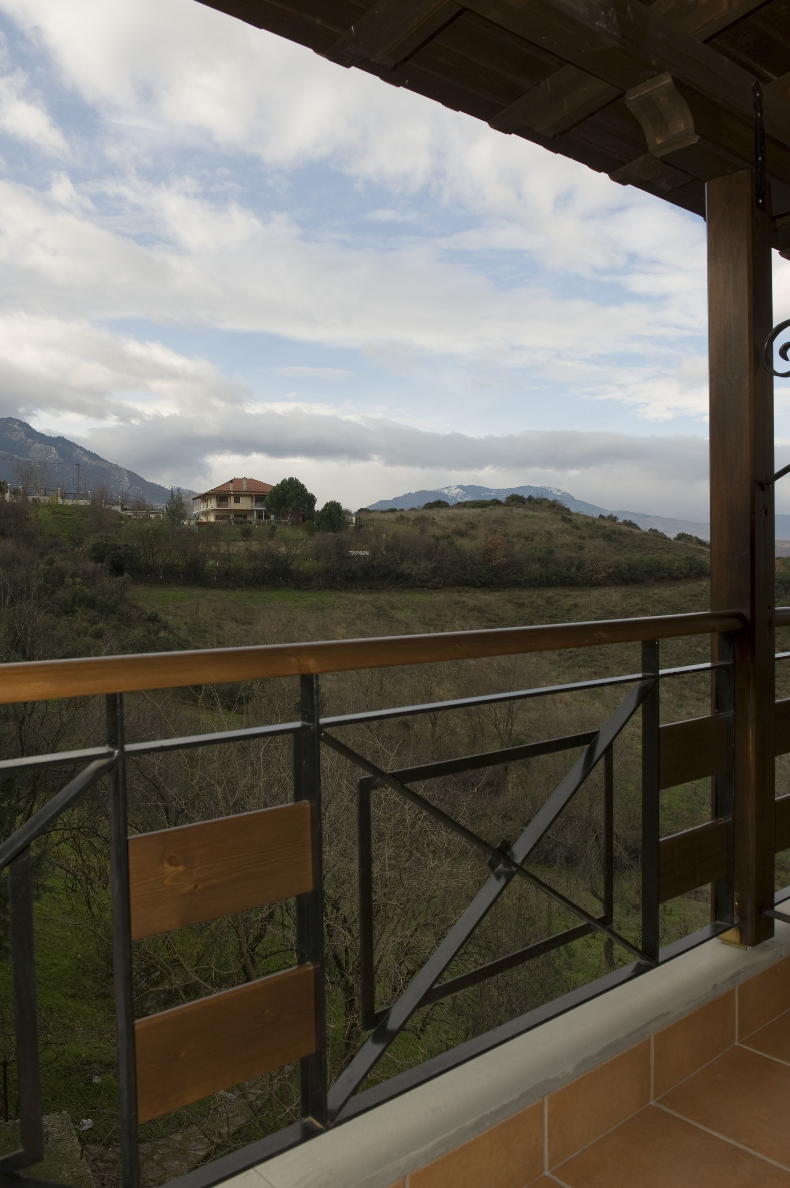 Un balcón con vista a una casa en una colina, barandilla metálica y cielo nublado.