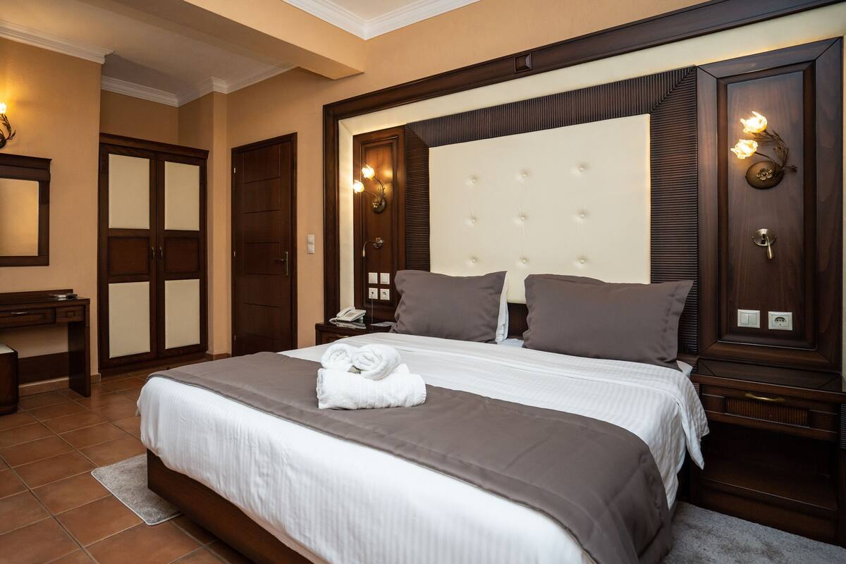 A hotel room with a large bed, a desk, and a wardrobe.