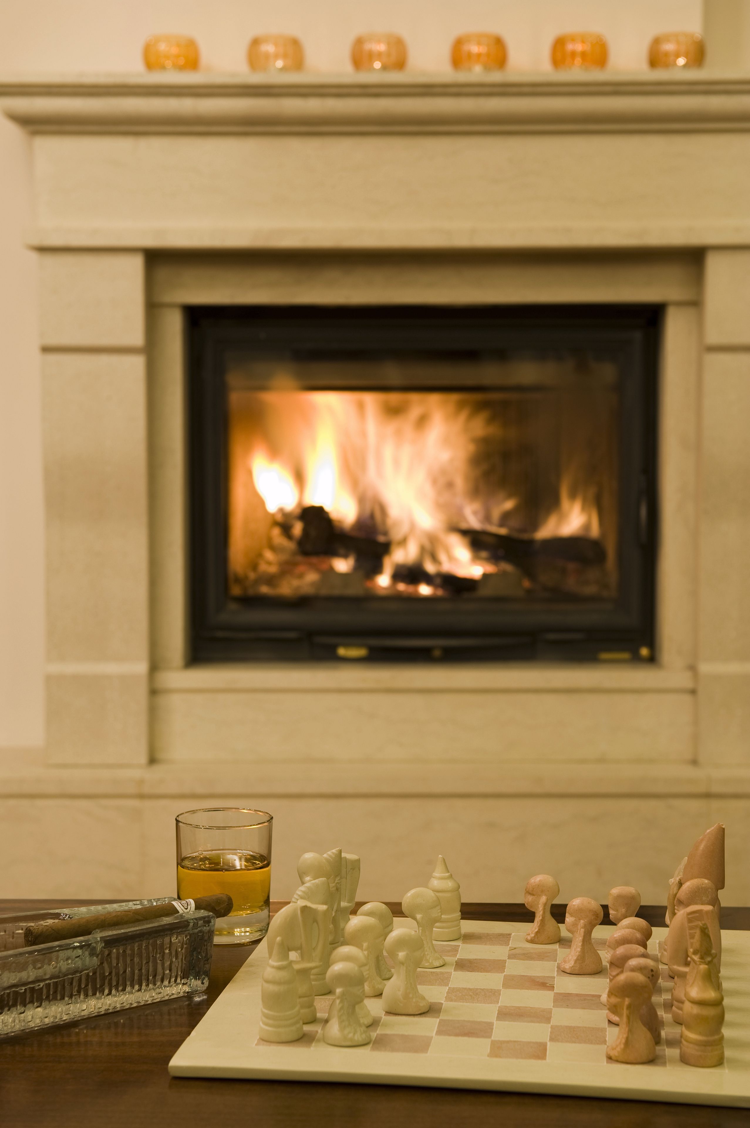 Une cheminée avec un feu de bois, un jeu d’échecs et un verre de whisky posés sur une table.