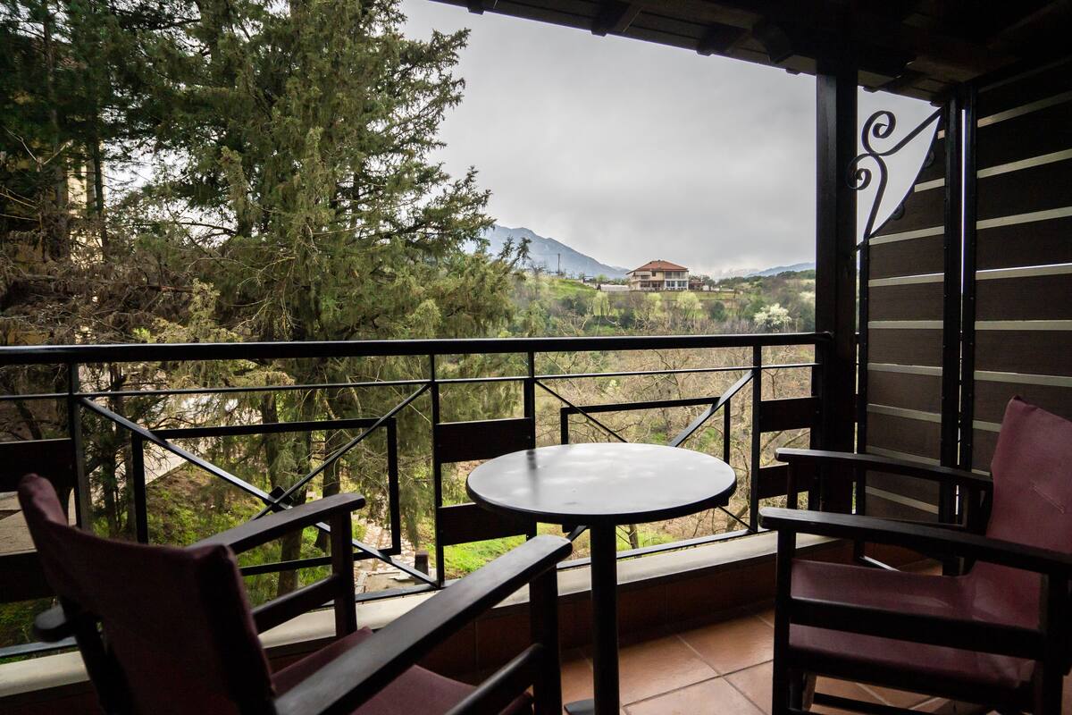 A balcony with a table and chairs, overlooking a mountainous landscape.