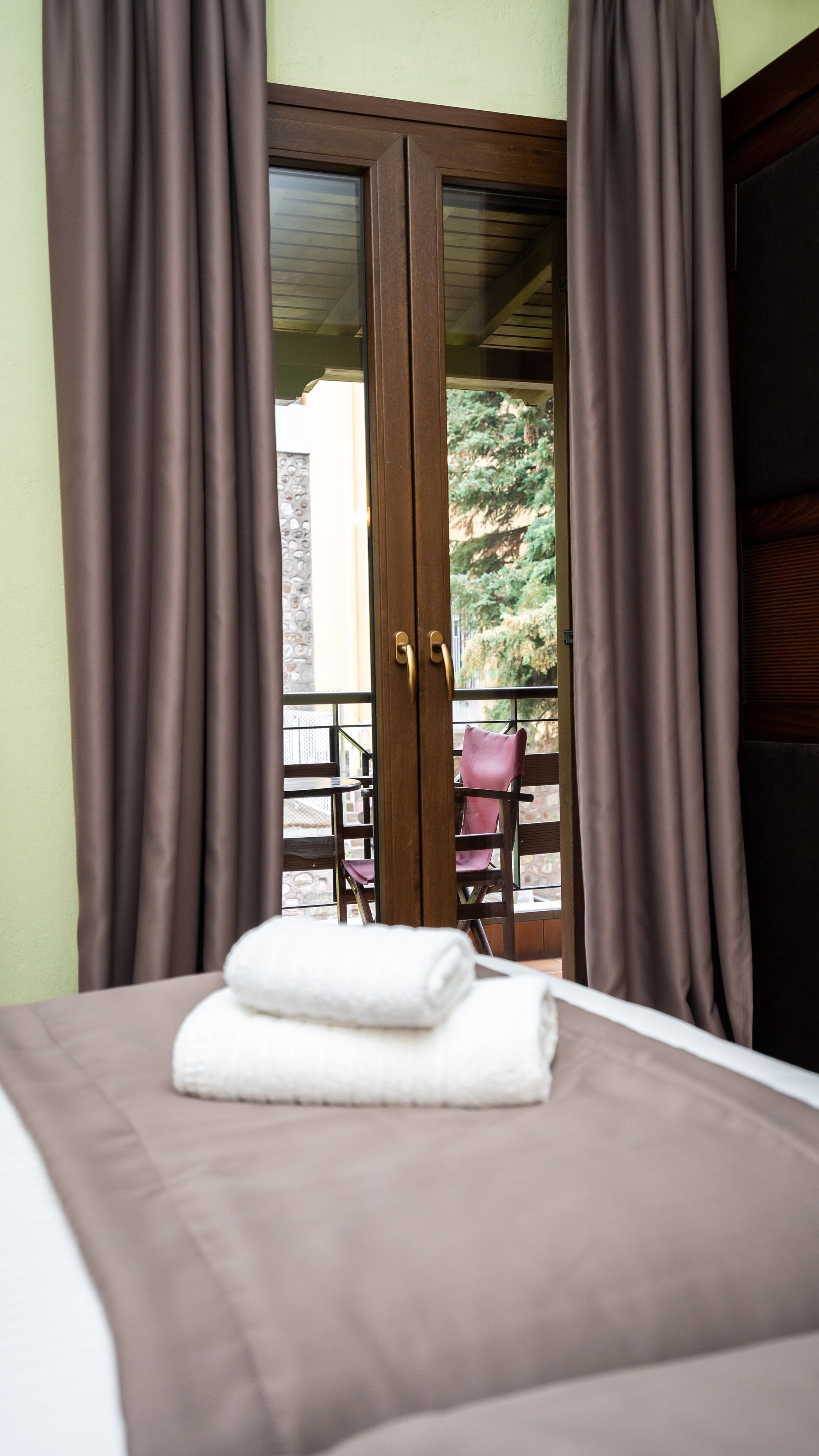 A hotel room with a bed, a balcony with a table and chairs, and brown curtains.