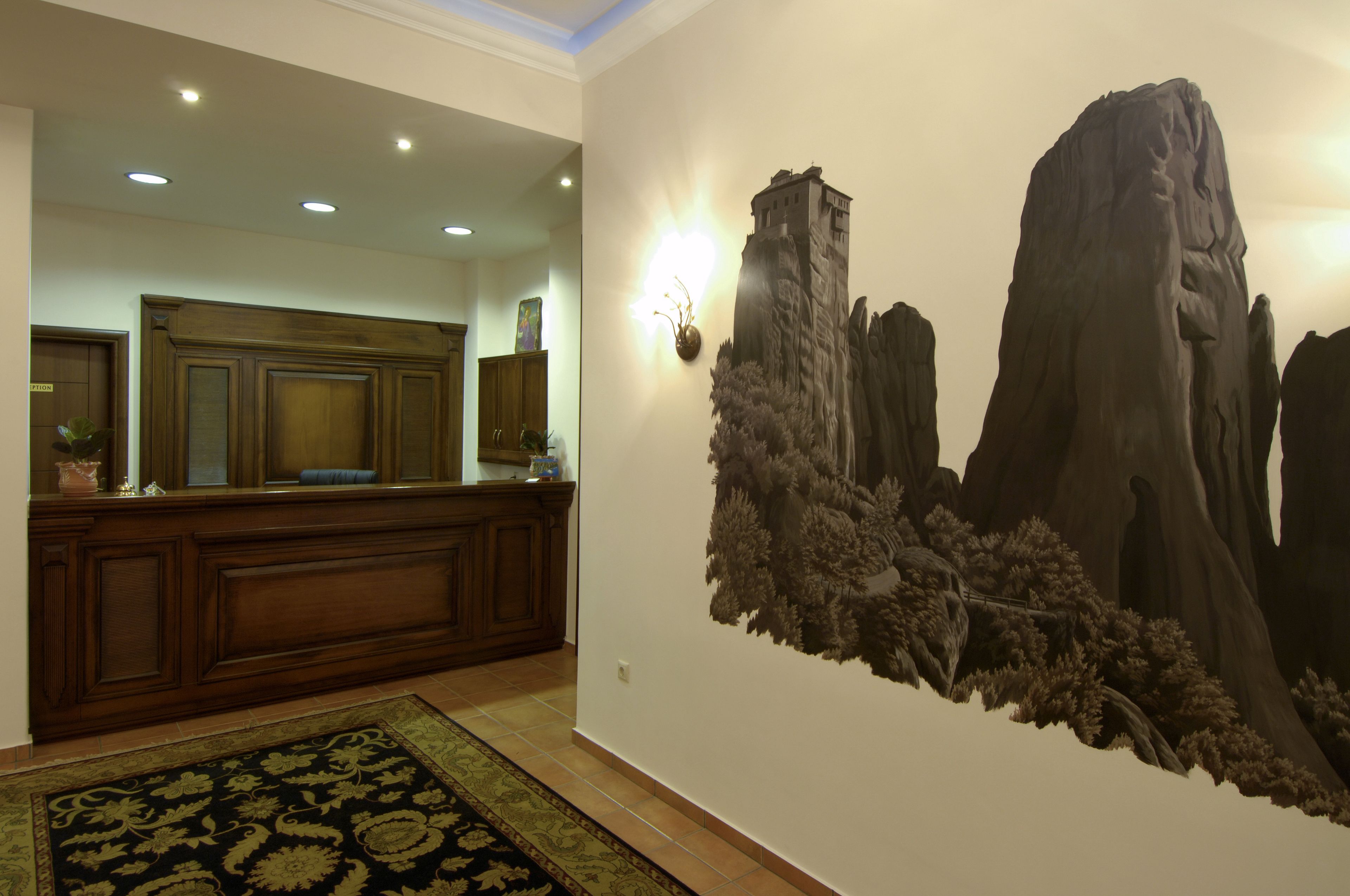 A reception area with a wooden reception desk, a wall-mounted light fixture, and a large wall mural of a mountainous landscape.