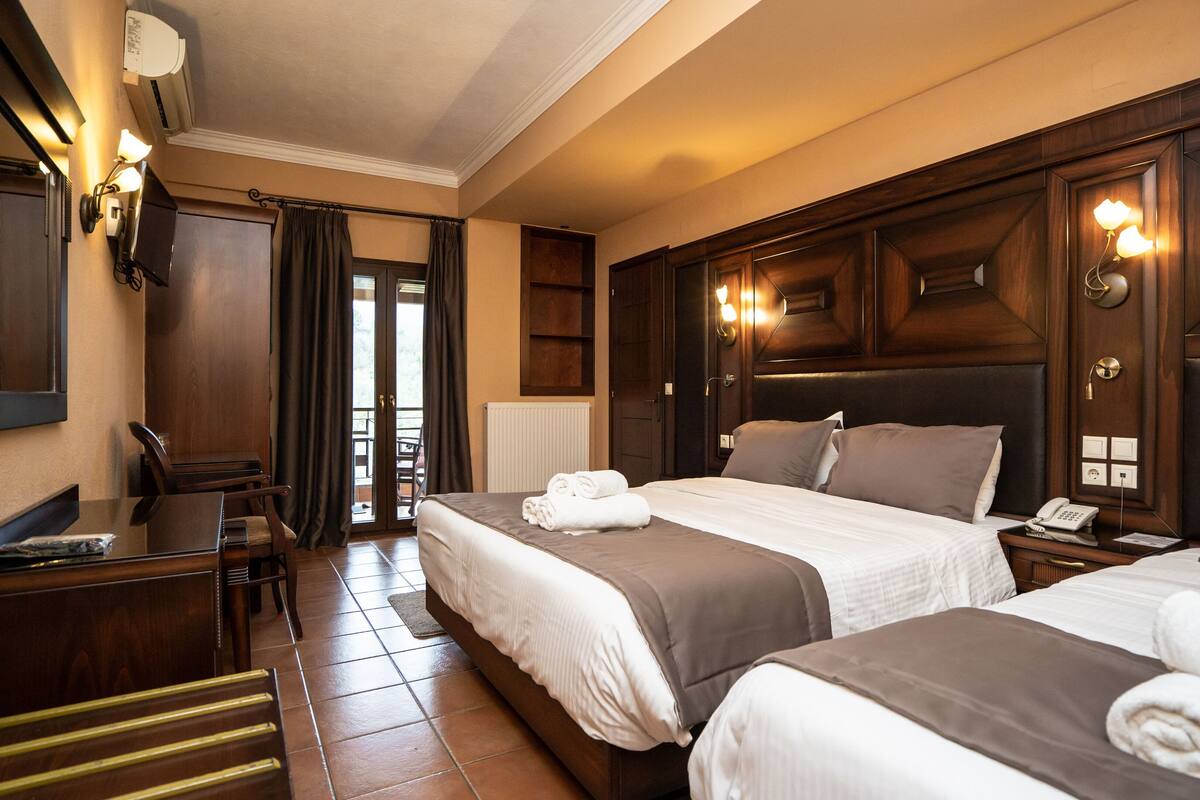 A hotel room with two beds, a desk, a chair, and a view of the outdoors.
