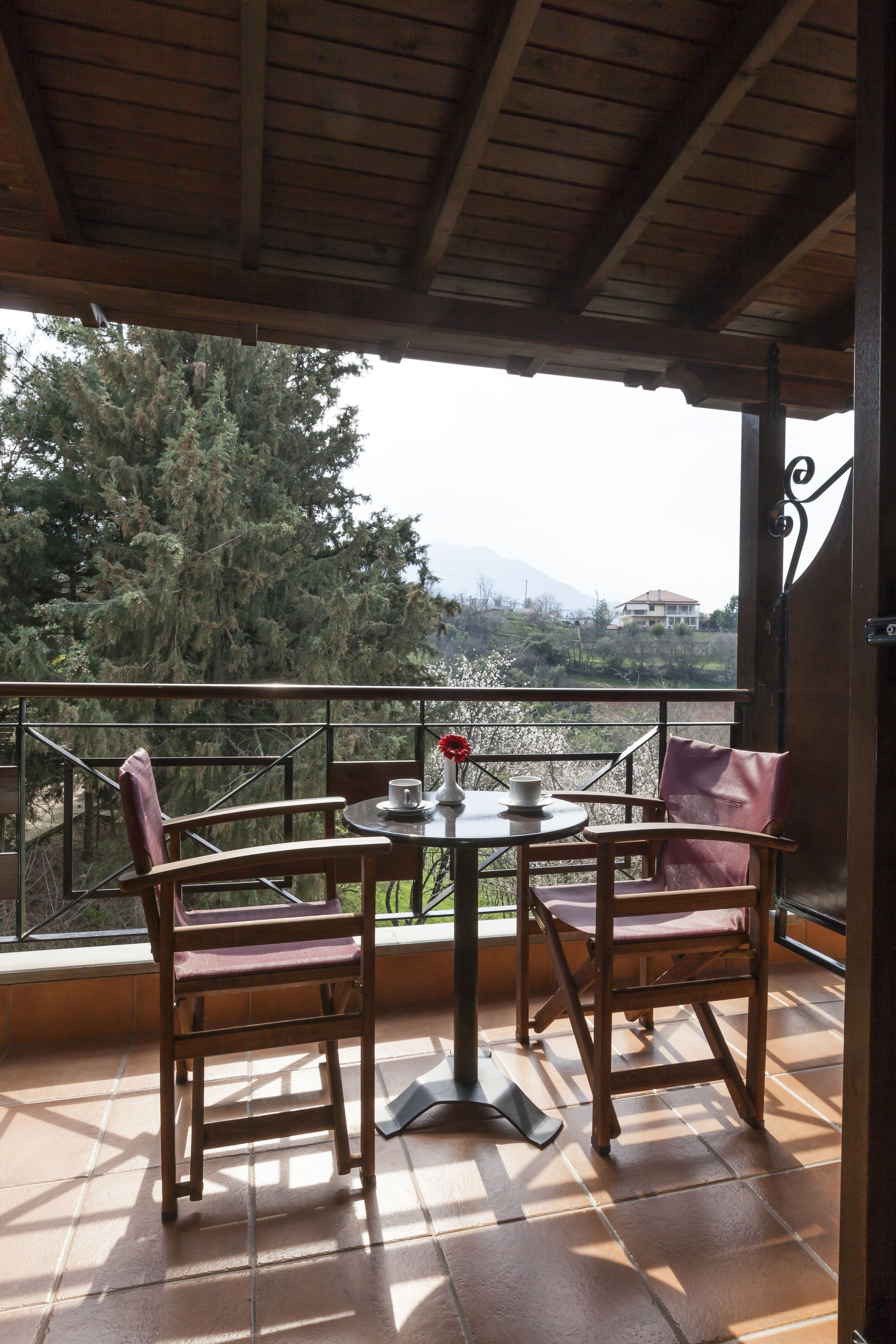 A covered outdoor seating area with two wooden chairs and a table, overlooking a mountainous landscape.