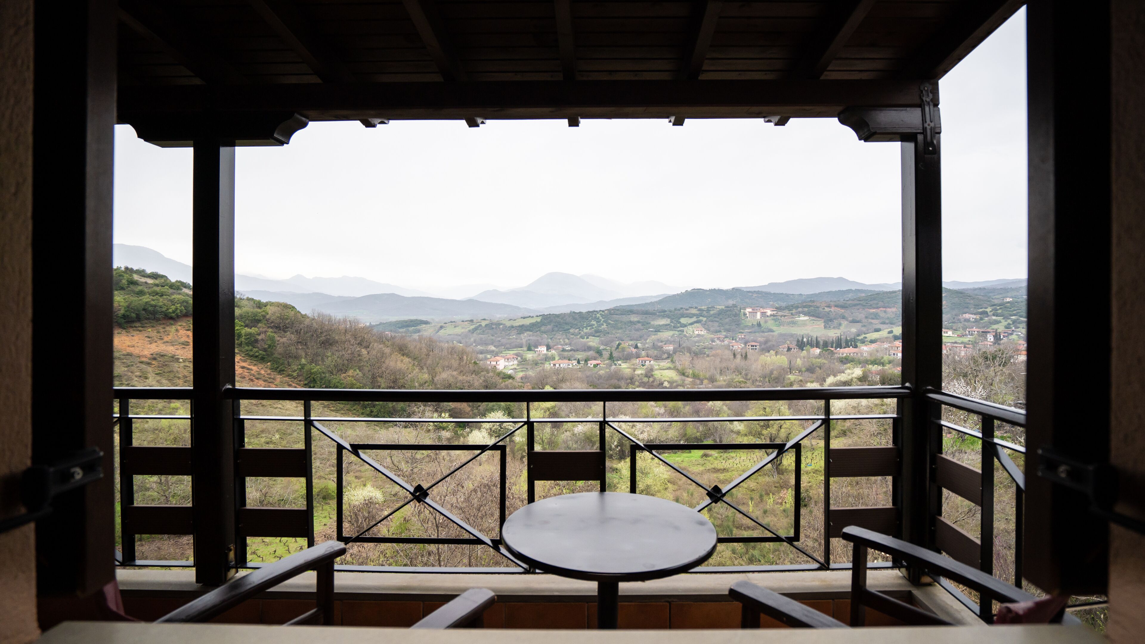 A balcony with a table and chairs, overlooking a mountainous landscape with houses.