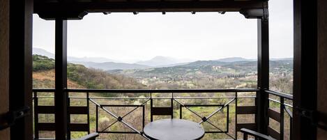 A balcony with a table and chairs, overlooking a mountainous landscape with houses.
