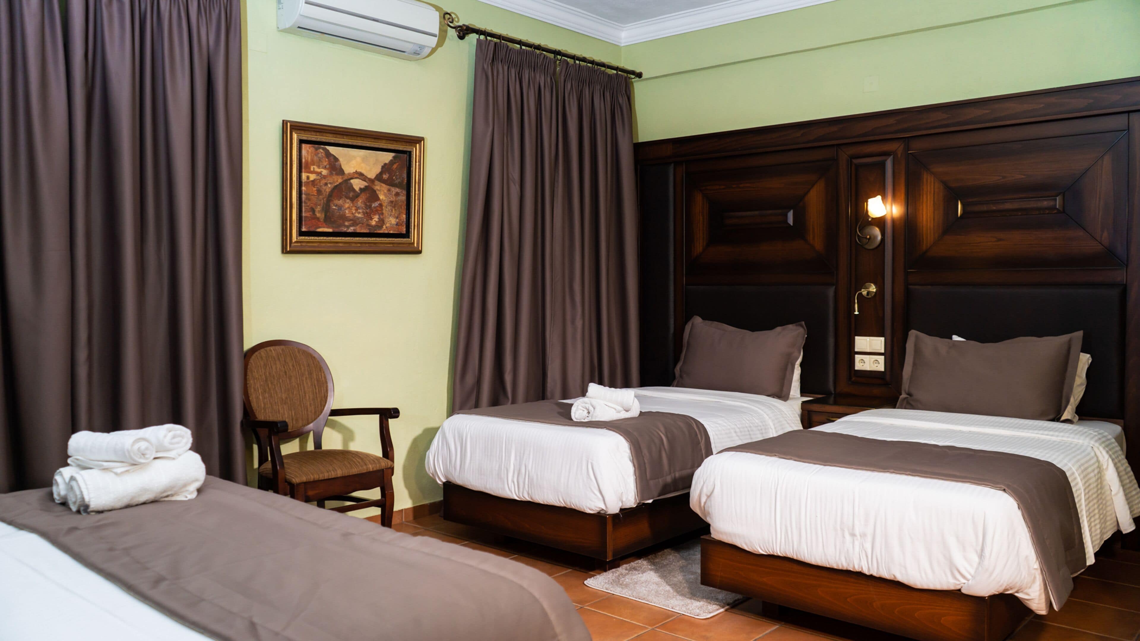 A hotel room with two beds, a chair, and a painting on the wall.