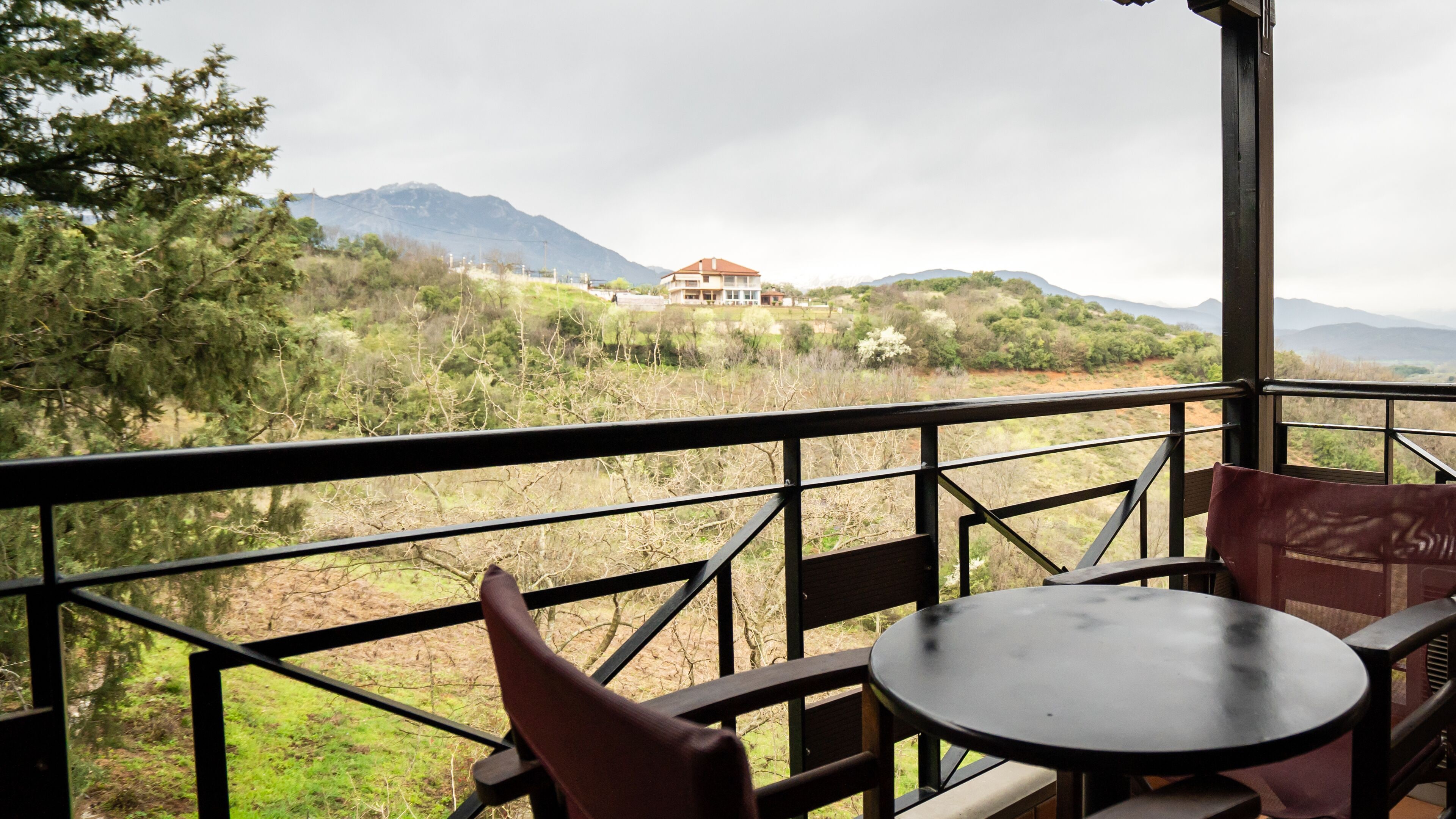 Een balkon met tafel en stoelen met uitzicht op een bergachtig landschap en een gebouw.