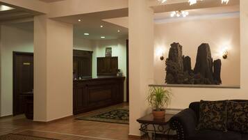 A lobby with a reception desk, a dark-colored sofa with patterned cushions, a potted plant, and a wall-mounted artwork depicting rock formations.