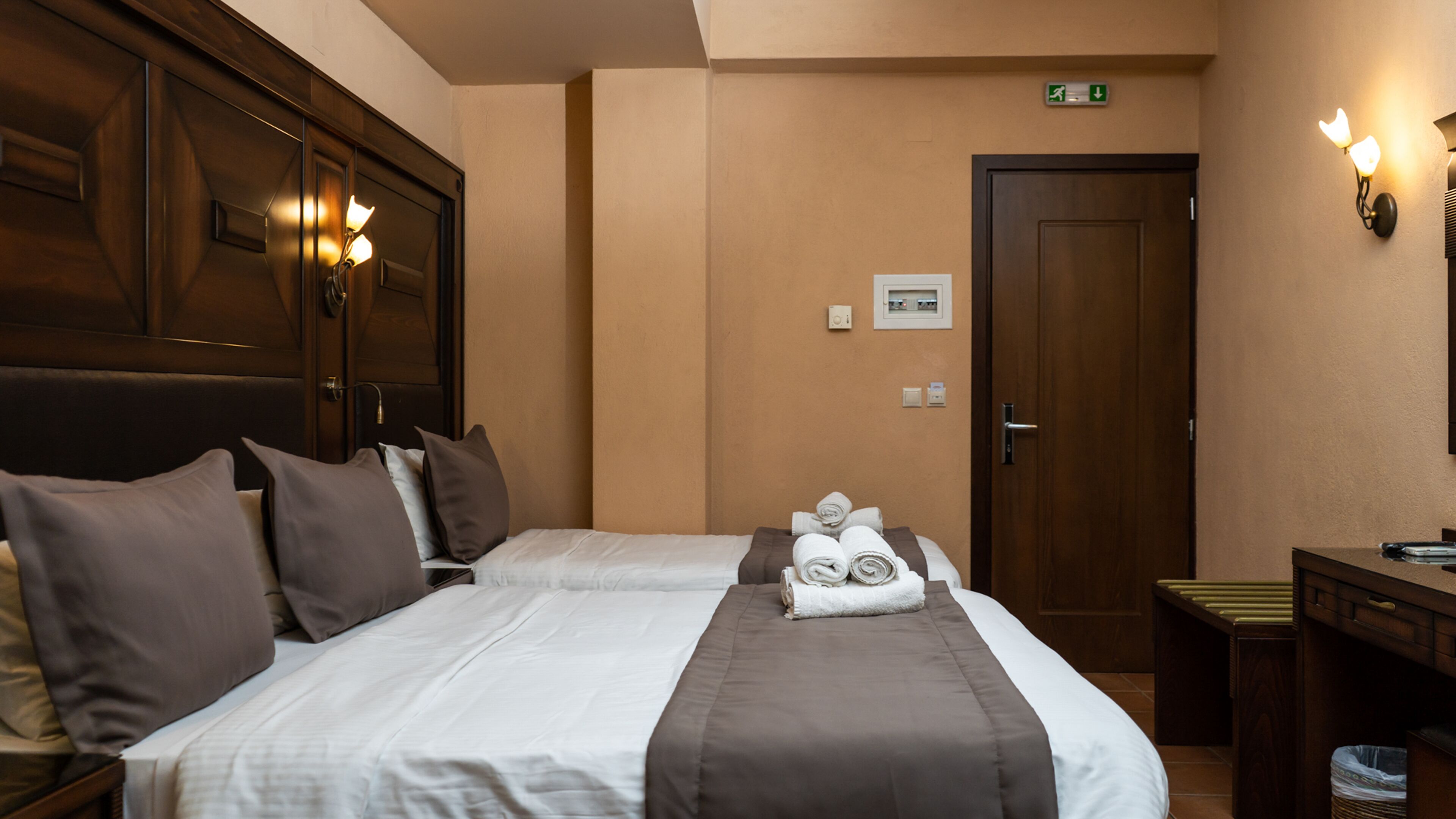 Habitación de hotel con dos camas, cabecero de madera, escritorio y un cubo de basura.