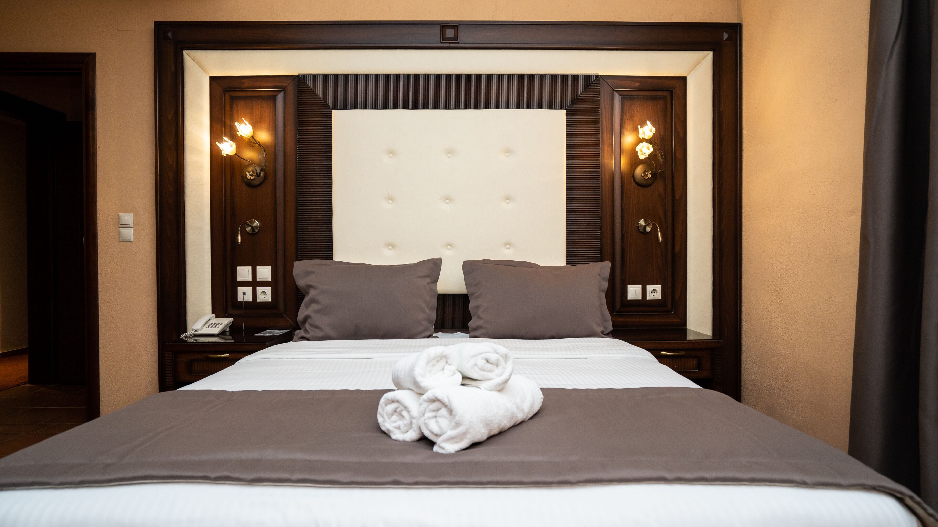 Une chambre d’hôtel avec un grand lit, deux oreillers, une serviette soigneusement pliée et une table de chevet avec un téléphone et une lampe.