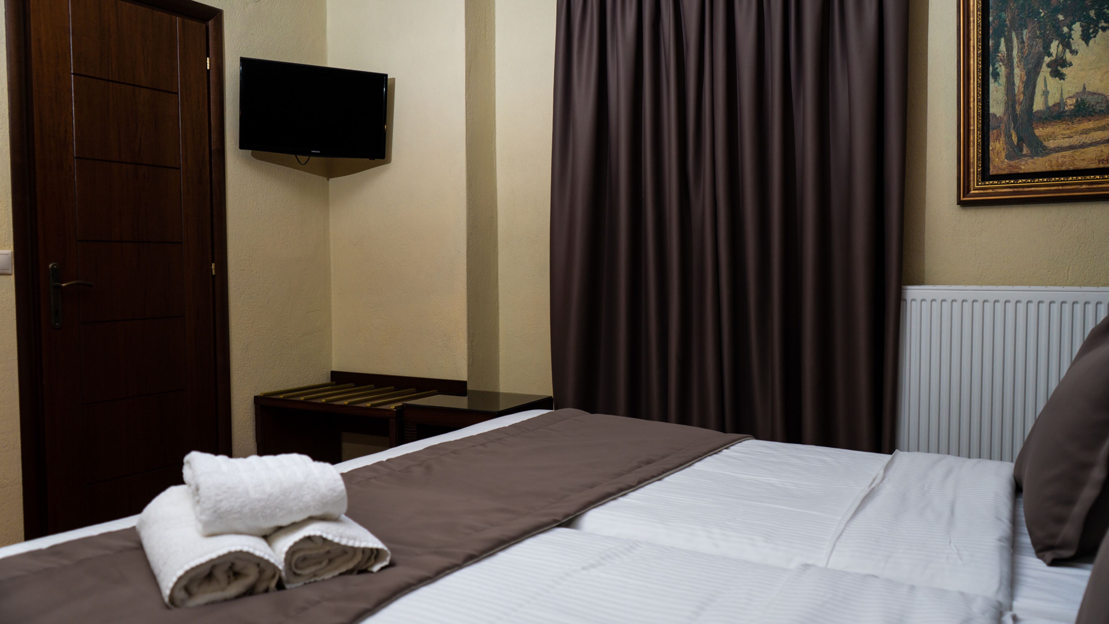 Habitación de hotel con cama, televisor montado en la pared, radiador y un cuadro.