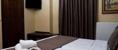 A hotel room with a bed, a TV mounted on the wall, a radiator, and a painting on the wall.