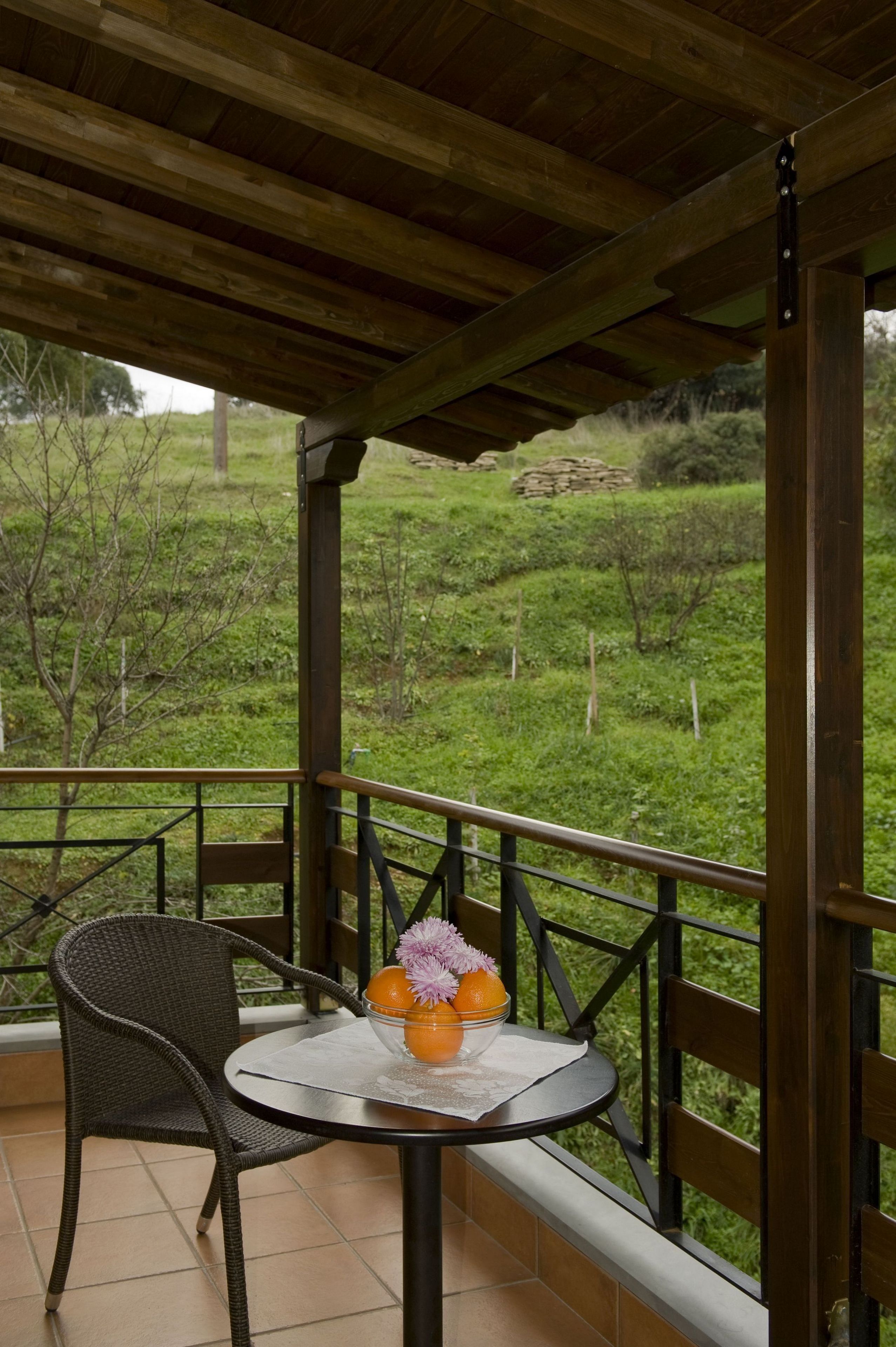 A balcony with a wicker chair and a small table with a vase of flowers.