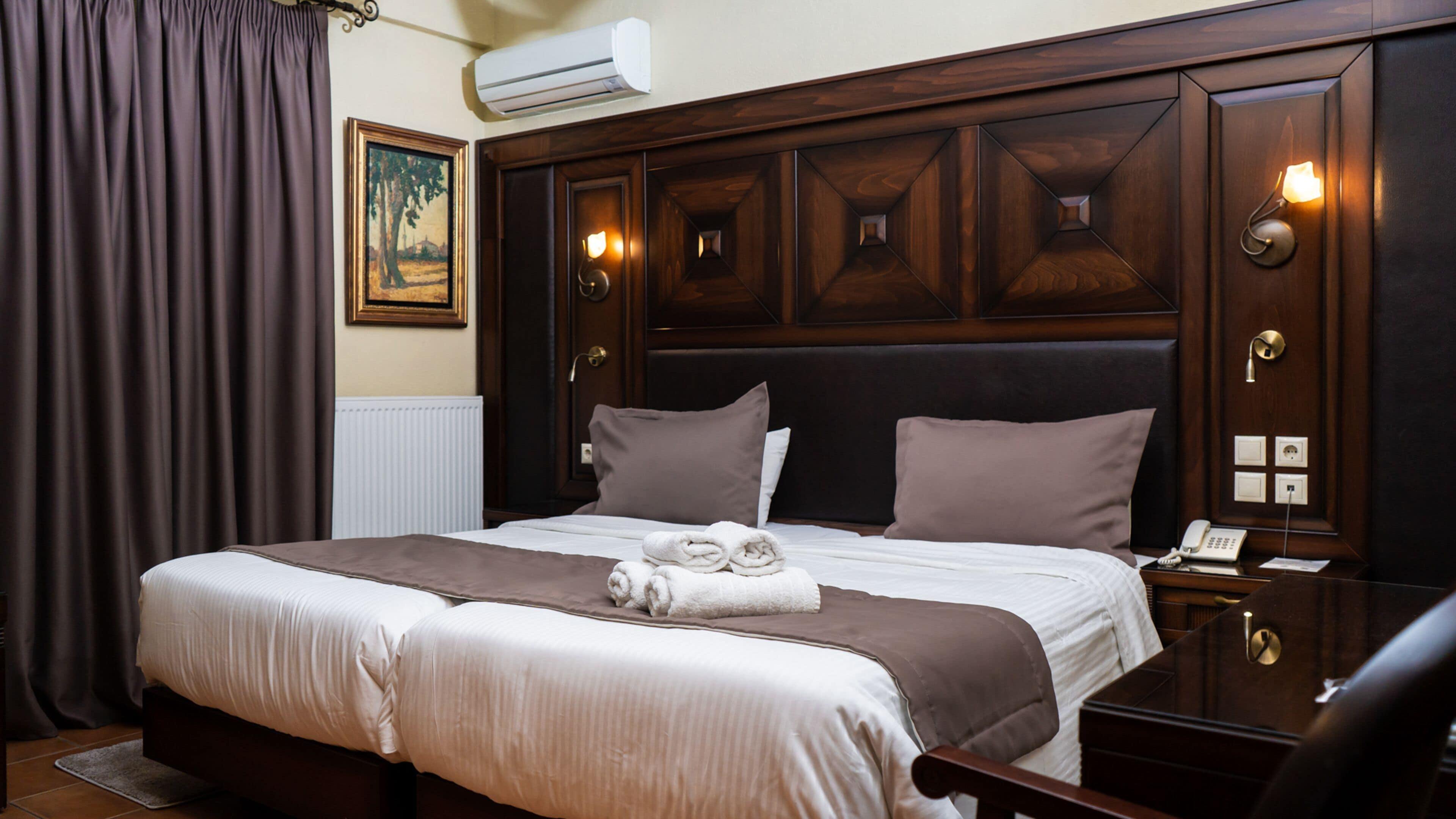 A hotel room with a large bed, a wooden headboard, a painting on the wall, and a telephone on the nightstand.