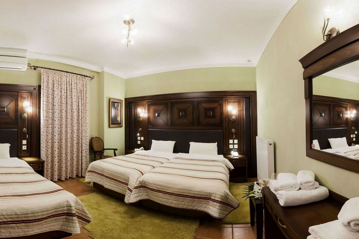A hotel room with two beds, a television, an air conditioner, a mirror, and a bathroom with towels.