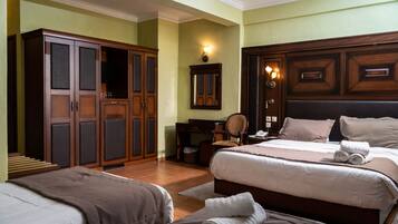 Une chambre d’hôtel comprenant une grande armoire, un bureau avec une chaise, un lit avec deux oreillers et une table de chevet avec une lampe.