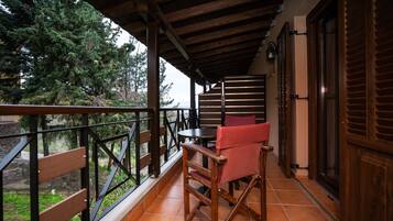 A balcony with a wooden table and red chairs, a view of trees, and a wooden door.