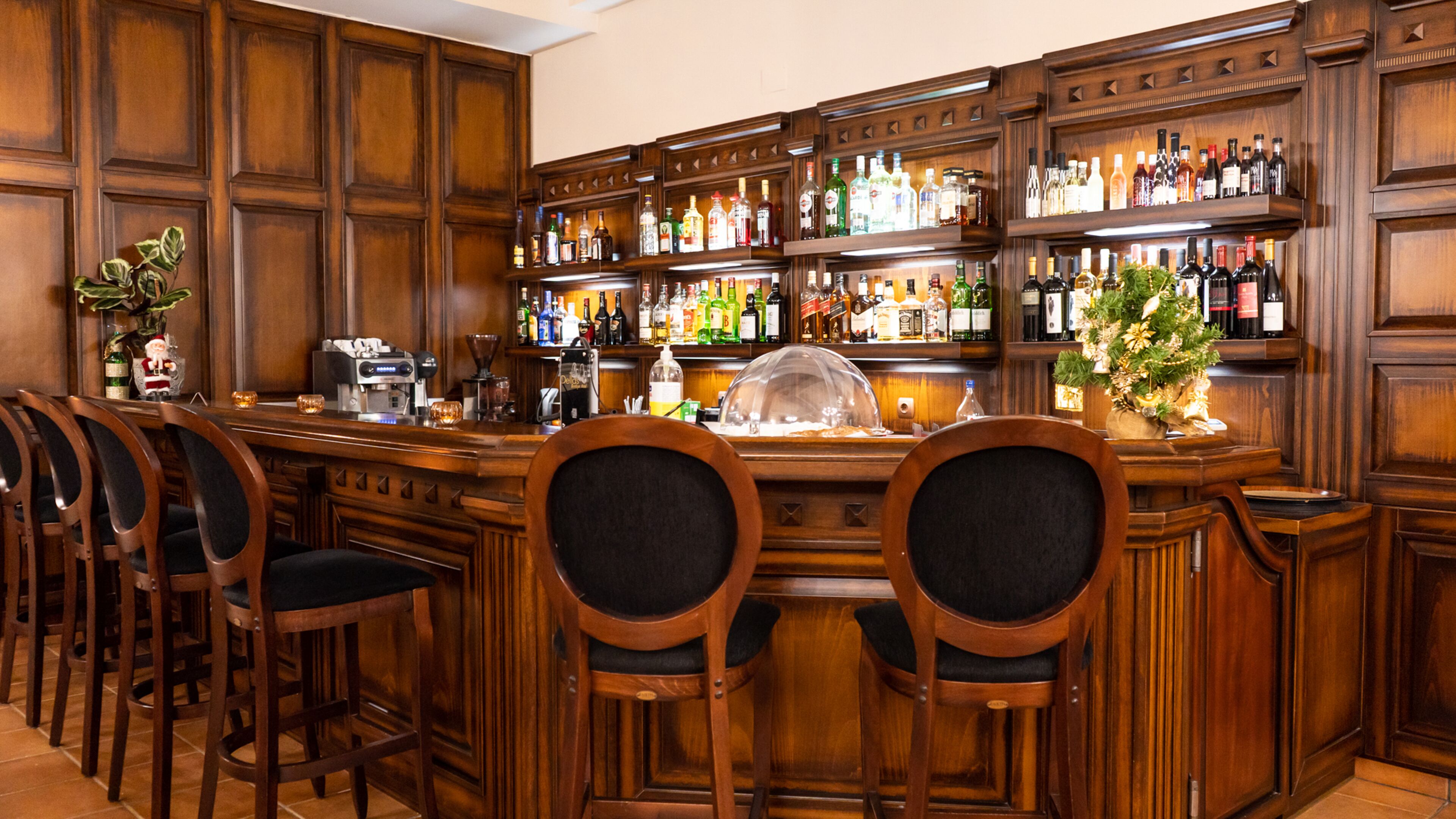 A bar area with wooden paneling, multiple liquor bottles, a coffee machine, and bar stools.