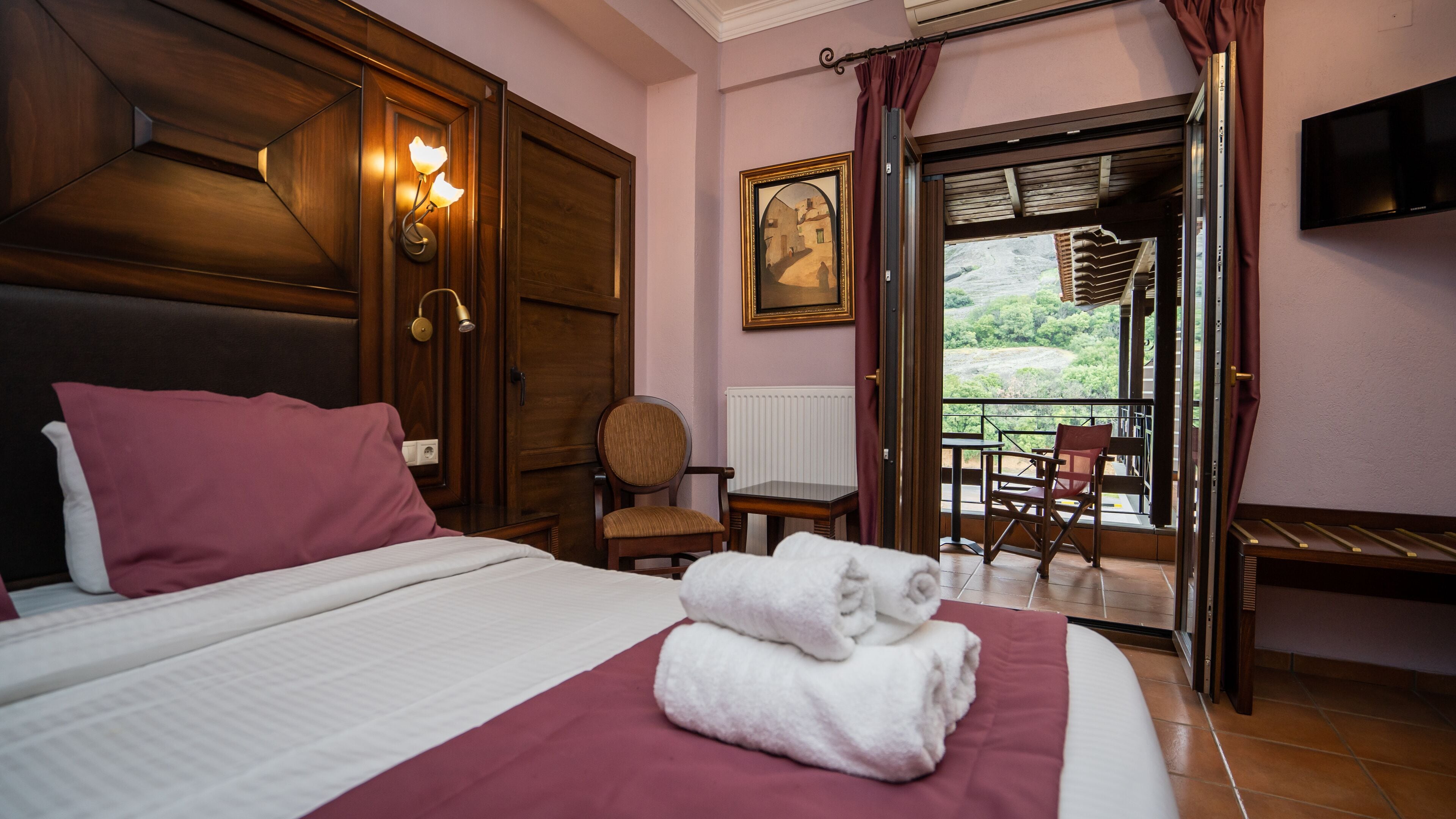 Habitación de hotel con cama, una silla, una mesa, un cuadro y un balcón con vistas.