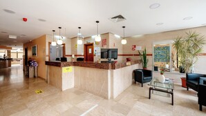 A hotel reception area with a marble counter, black sofas, a glass coffee table, and potted plants. - Hotel Avenida Praia (Portimão)