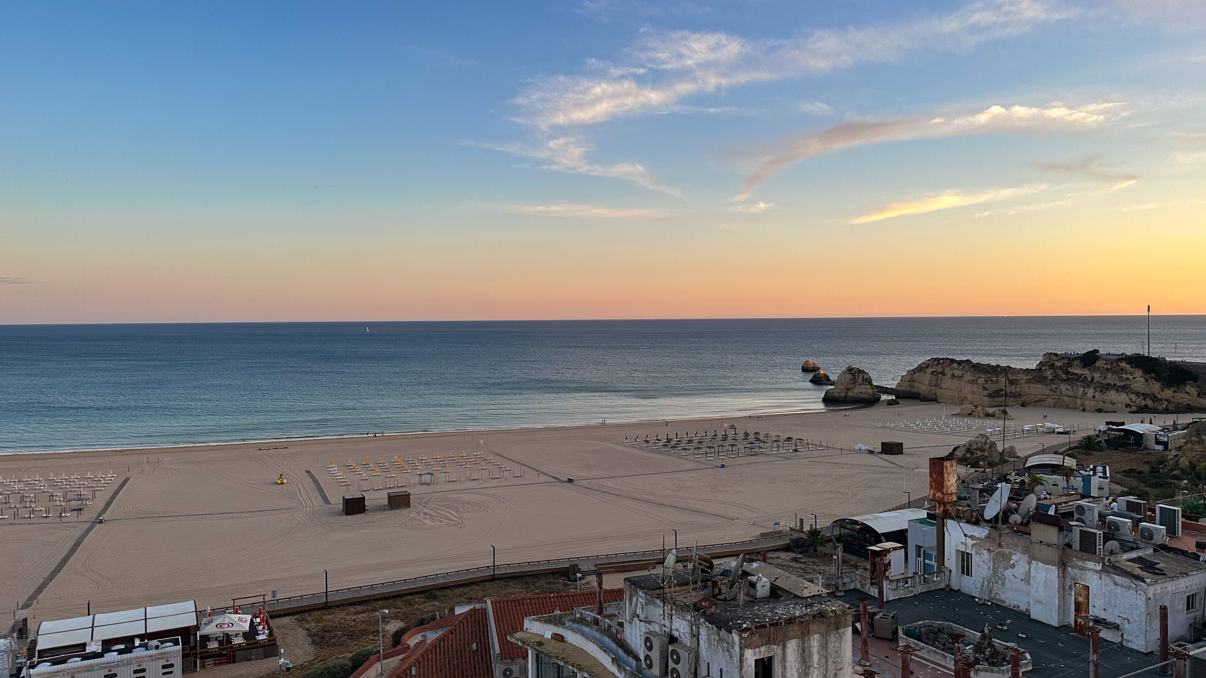 Platja amb cel serè, una roca i una filera d'edificis amb antenes satèl·lits.