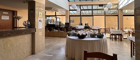 A hotel lobby with a reception desk, a buffet table with food items, and a seating area with tables and chairs.