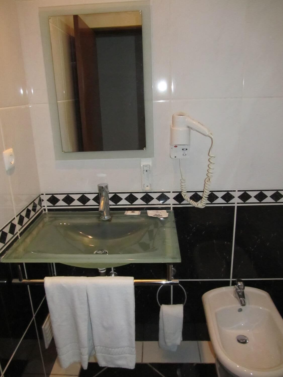 Une salle de bain équipée d’un lavabo en verre, d’un miroir, d’un sèche-cheveux, d’un bidet et de serviettes.
