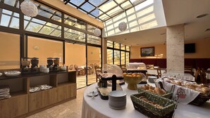 A hotel dining area with a buffet setup, including bowls of food, plates, and a variety of bread. - Hotel Avenida Praia (Portimão)