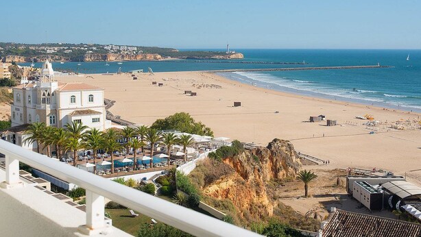 A beach resort with a large building, palm trees, and a view of the ocean. - Hotel Avenida Praia (Portimão)