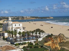 Um hotel à beira-mar com uma praia extensa, área de piscina e um edifício imponente com torre.