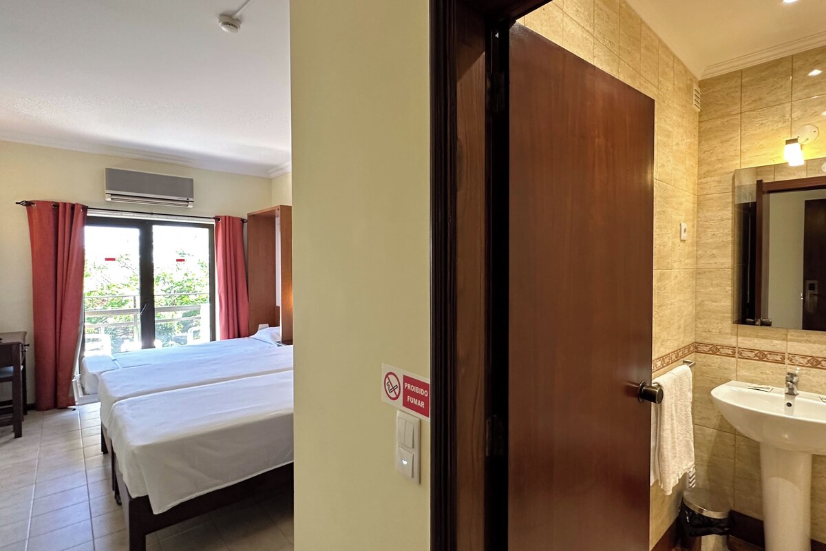 A hotel room with a bed, a desk, a bathroom with a sink and mirror, and a sign prohibiting smoking.