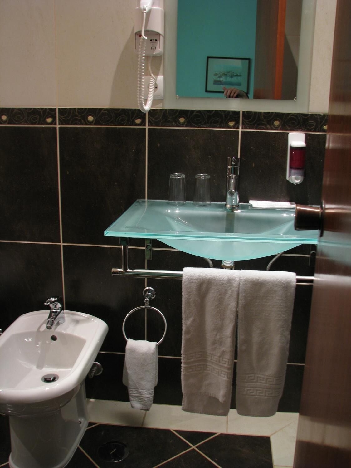 A bathroom with a glass sink, a bidet, and a towel rack with two towels.