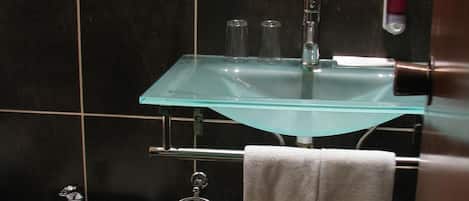 A bathroom with a glass sink, a bidet, and a towel rack with two towels.