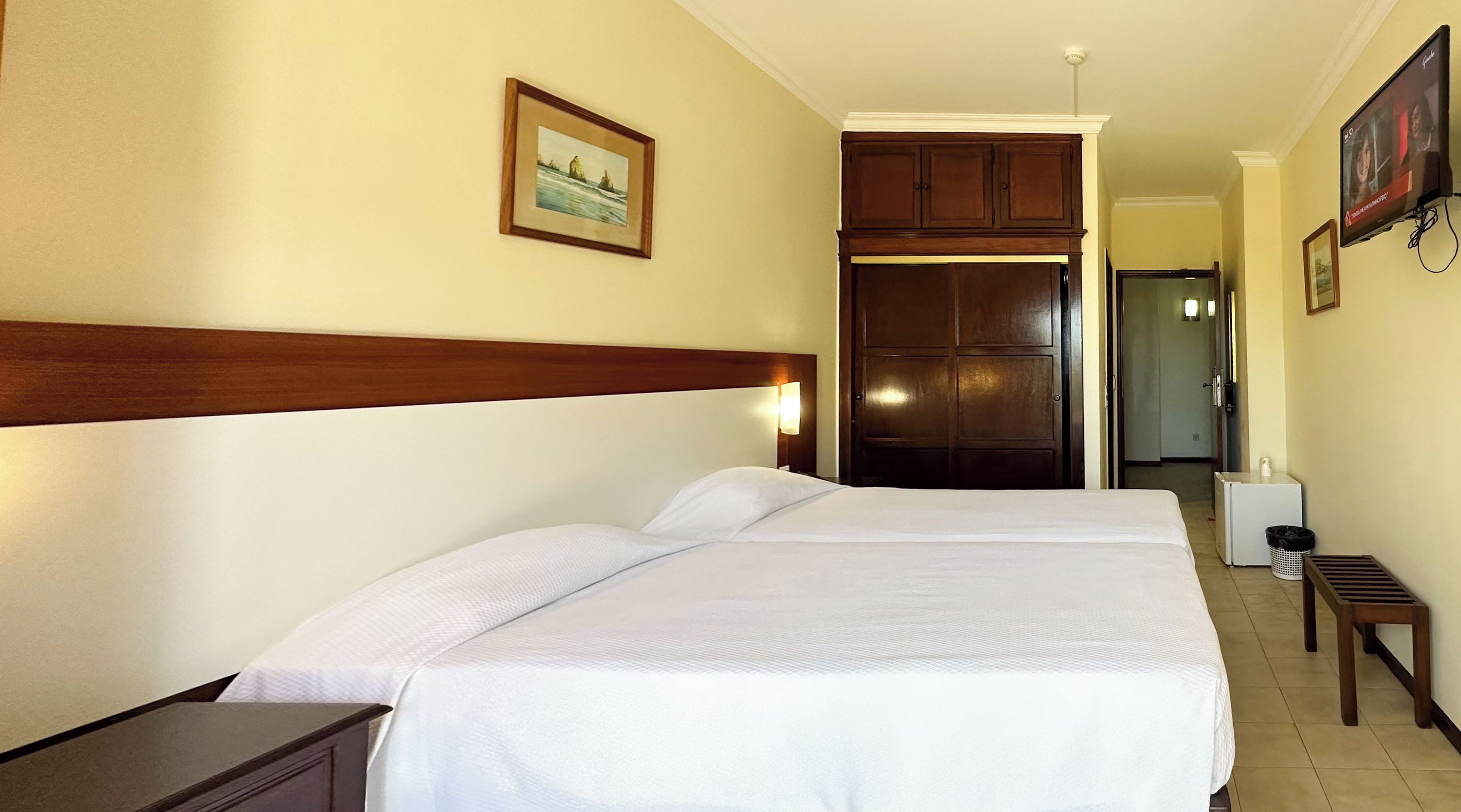 A hotel room with a bed, a nightstand, a dresser, a painting on the wall, and a television.