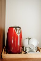 A red kettle on a wooden tray with white dishes stacked beside it.