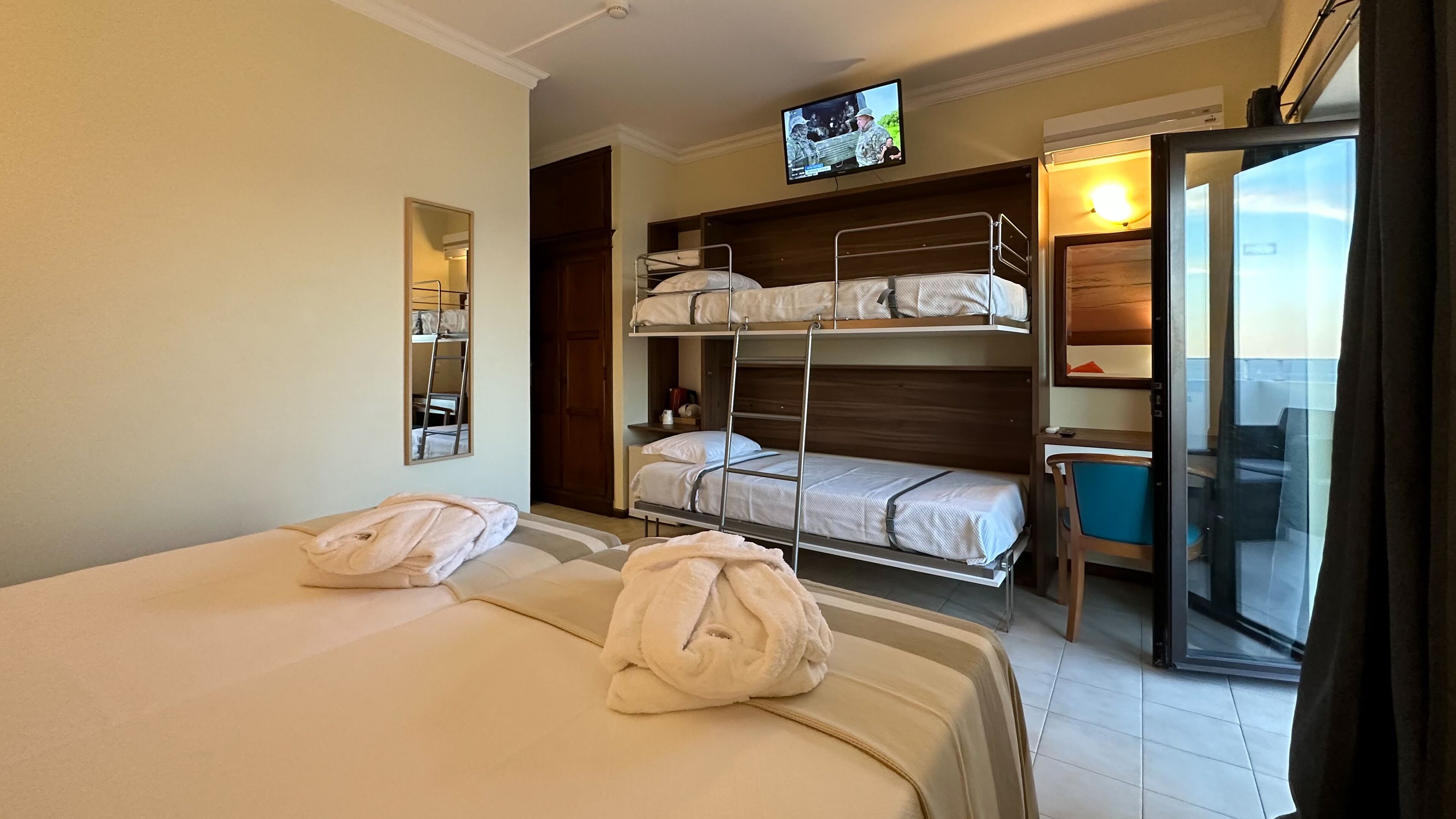 Habitación de hotel con dos camas, televisión, espejo y balcón con vistas.