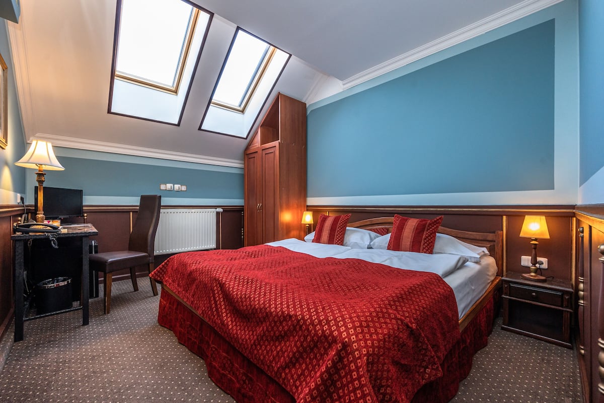 Habitación de hotel con cama, escritorio, silla y radiador. Hay tragaluces en el techo.