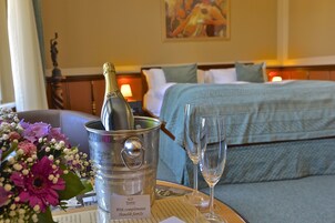 Una camera d'albergo con un letto, un comodino con una bottiglia di champagne e calici, e un bouquet di fiori.