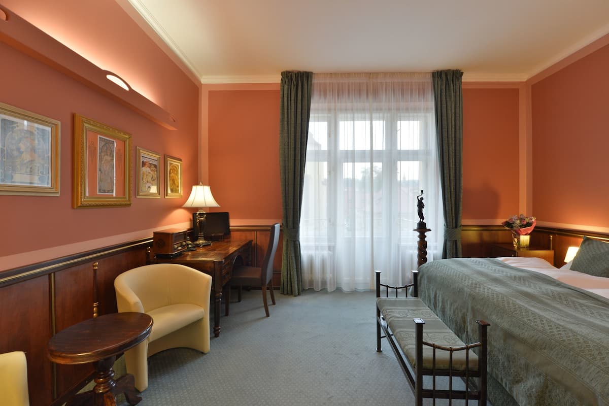 Una habitación de hotel con cama, escritorio, silla y ventana con cortinas.