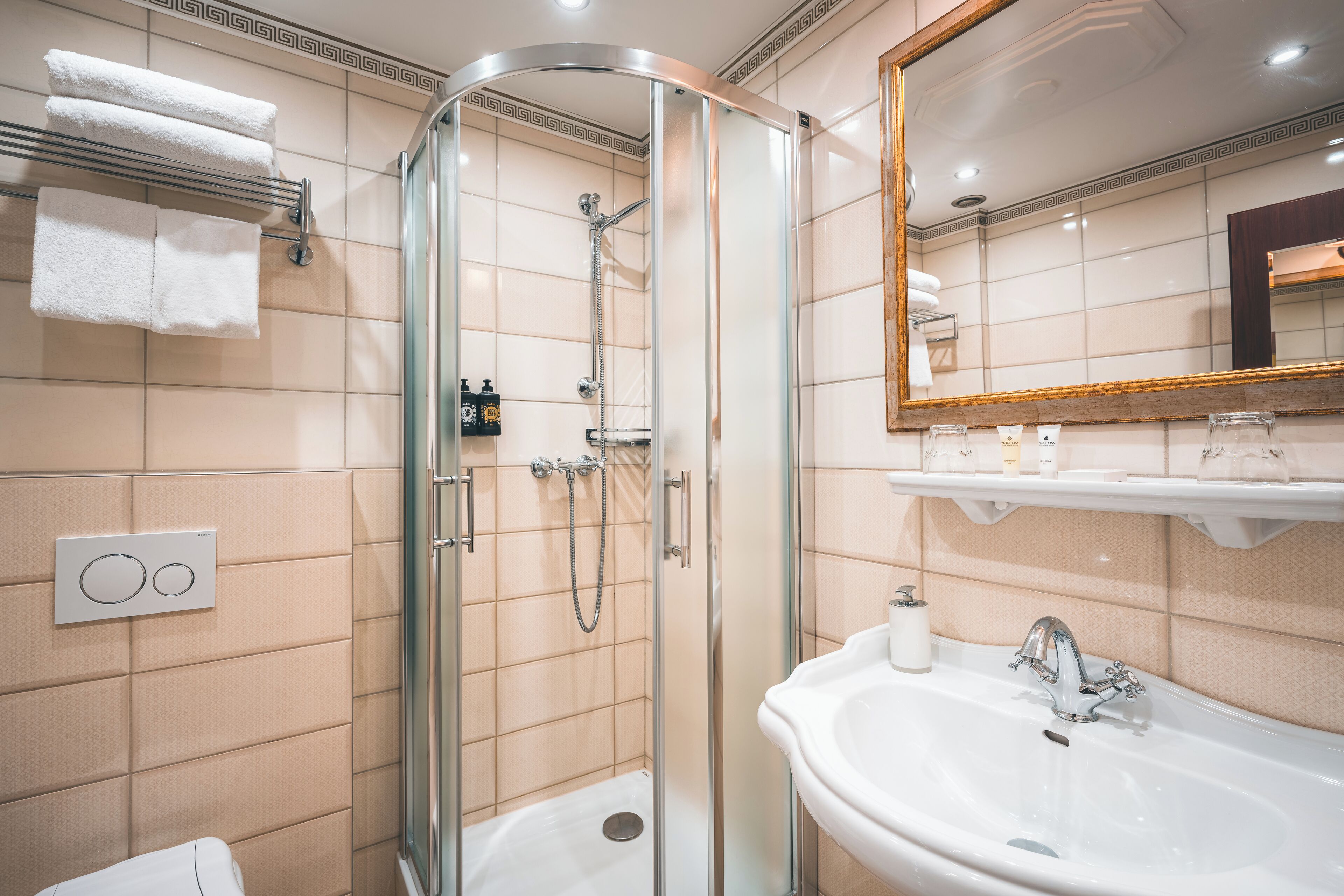 Un baño moderno con ducha envuelta en vidrio, un lavabo blanco y un espejo con marco de madera.