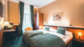 Quarto de hotel com duas camas, uma escrivaninha com abajur, uma cadeira e um quadro na parede.