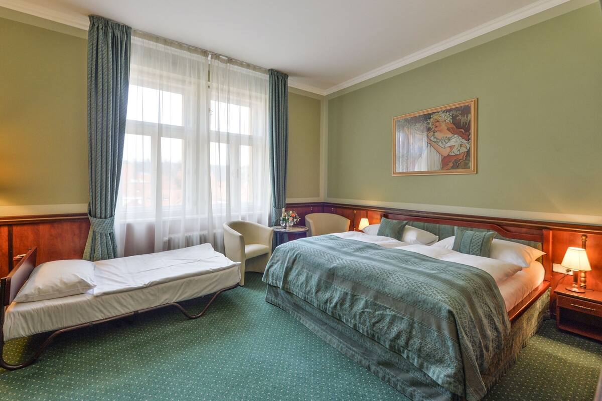 Una habitación de hotel con dos camas, una silla, una mesita de noche y un cuadro en la pared.