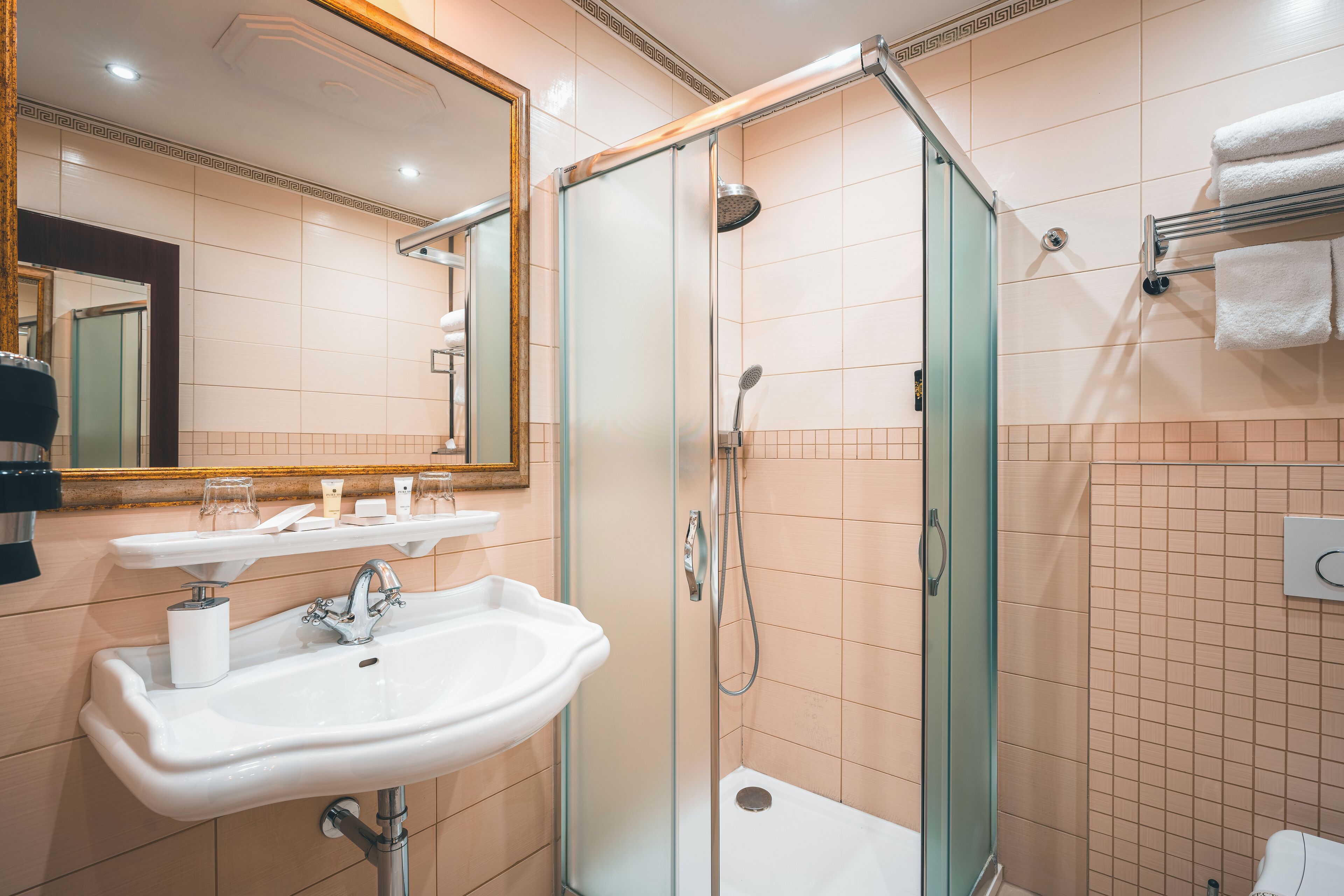 Un baño moderno con ducha acristalada, lavamanos blanco y un espejo grande.